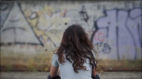 Sadness, depression - back view of young woman sitting in front of a mural Stock Footage 135425693