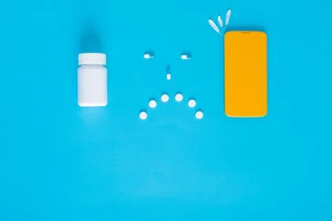 Safe self-isolation. sad smiley face with pills, phone on a blue background. Stock Photos