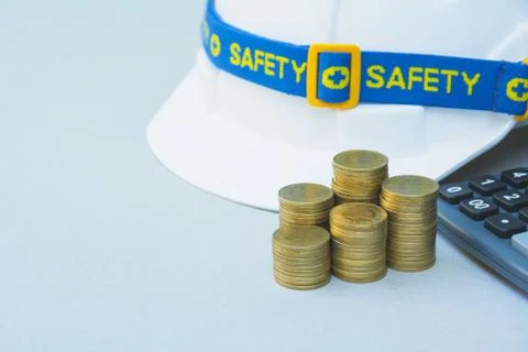 Safety engineer helmet with stack coins and calculator. Stock Photos