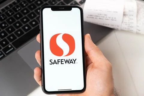 Safeway application on the screen of Apple iPhone in mans hand and laptop on the Stock Photos