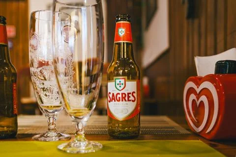 Sagres beer bottle on a table with empty beer glasses and a red heart-shape.. Stock Photos