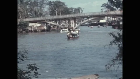 SAIGON - 1971: River traffic - Sampans on a city waterway beneath a footbridge 库存影片 343938363