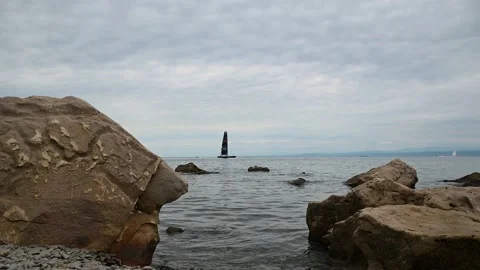 A sailboat appears from behind large rocks on the shore Stock Footage 202113358