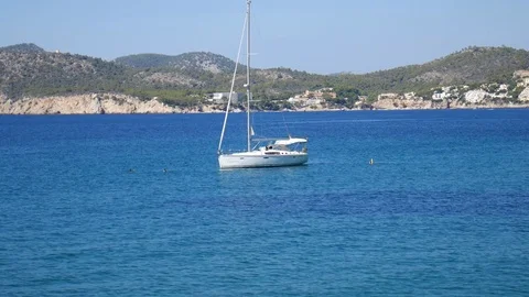 Sailboat floating on small waves on the blue sea with mountain landscape in Cala 库存影片 81047474