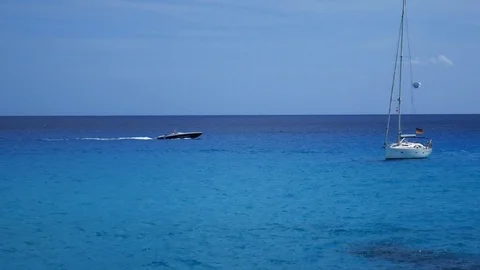 Sailboat floating on small waves on the blue sea with speeboat sailing past in Stockbeeldmateriaal 81048212