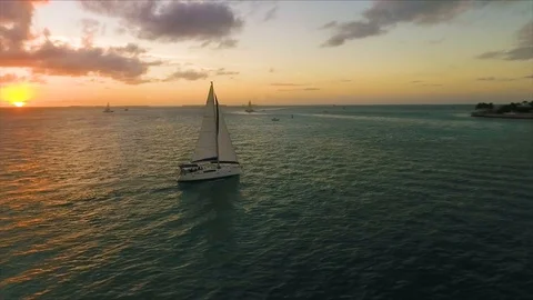 Sailboat floats as the sun sets while a drone orbit's around the boat in Video stock 106067276