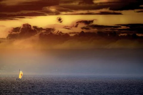 Sailboat navigates the ocean under a dramatic sunset sky with fiery clouds 写真素材