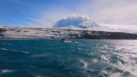 Sailboat navigating rough seas near an erupting volcano 스톡 동영상 335498253