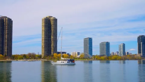 Sailboat sailing in river, surrounded huge skyscrapers. Calm day time on river Stock Footage 248375501