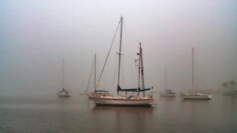 Sailboats anchored in thick grey foggy harbor in the morning Stock Photos