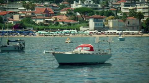 Sailboats floating on calm waters in front of a vibrant coastal town beach with Stock Footage 339815080