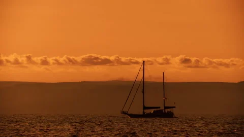 A sailing boat floats along the waves in the orange light of the evening sunset Stock Footage 92205658