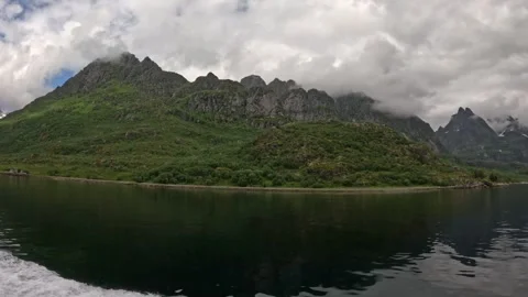 Sailing past dramatic jagged mountain peaks shrouded in low clouds in Lofoten Stock Footage 344753156