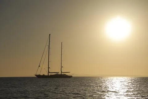Sailing ship with lowered sails in the sunset with huge sun in the golden hour. Stock Photos
