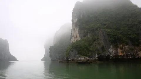Sailing through limestone islets in Ha Long Bay in thick fog. 库存影片 74327703