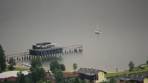 Sailing on a tranquil lake with a dock and distant houses under a serene sky Stock Footage 318079128