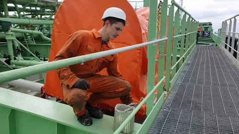 Sailor in orange uniform paints railing sitting on haunches Stock Footage 121118093