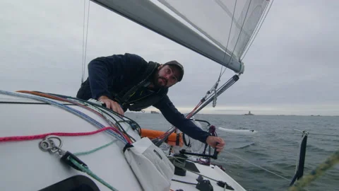 A sailor turns the crank to steer the sail of his sailboat, in Brittany, France Stock Footage 229738216