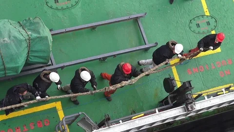 Sailors in helmets pull mooring end for fastening on bollard Stock Footage 121116457