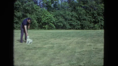 SAINT PAUL MINNESOTA-1963: Tiny White Dog With A Man Dressed In Black Playing Video stock 123808901