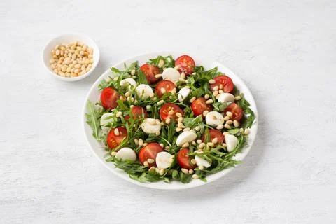 Salad with arugula, cherry tomatoes, mini mozzarella and pine nuts on a lig.. Stock Photos