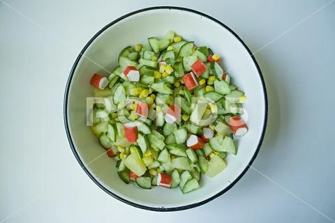 Salad with corn, crab sticks, cucumbers in a white bowl on a white background Stock Photos