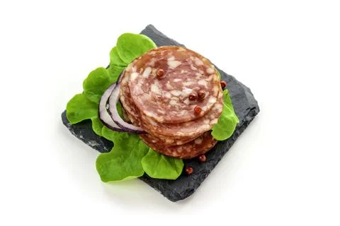 Salami sausage eats on a black slate plate with lettuce, spices . Stock Photos