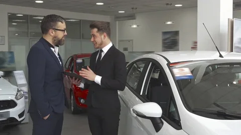 Sales manager explaines the contract to the customer at the car dealership 動画素材 76385332