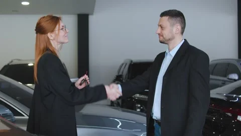 Sales representative hands over car keys to customer in auto dealership showroom Stock Footage 304716305