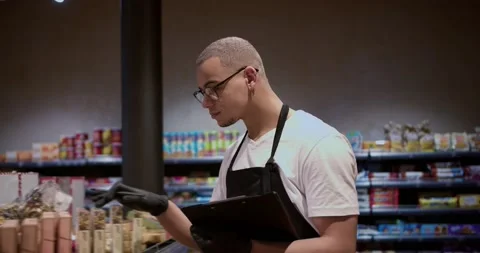 Salesman in apron using tablet counting goods in supermarket, regular inventory Видео 235348161