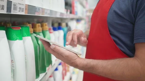 Salesperson hands using pc tablet in front of cleaners shelves in modern grocery Stock Footage 92210396