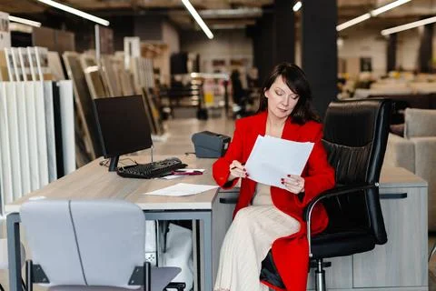 Saleswoman analyzing documents while sitting at desk in furniture store Stock Photos