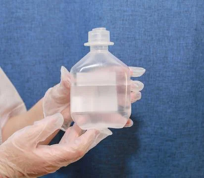 Saline solution in clear jar in hands of nurse wearing clear gloves Stock Photos