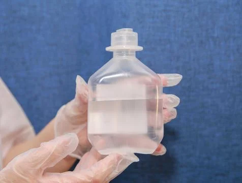 Saline solution in clear jar in hands of nurse wearing clear gloves Stock Photos