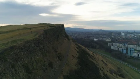 Salisbury Crags cliffs with walker walking down mountain, drone aerial 4K Stock Footage 101218783