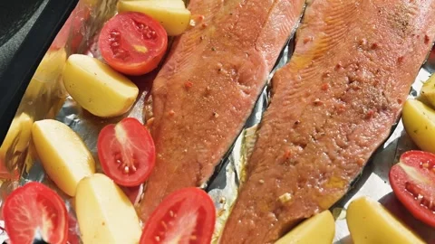 Salmon fillets are placed alongside sliced tomatoes and potatoes on a baking 库存影片 344667449