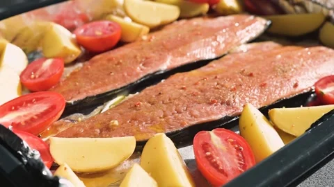 Salmon fillets are placed on a baking tray surrounded by sliced tomatoes and 库存影片 344667107