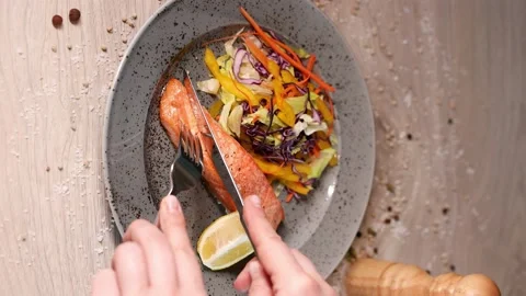 Salmon with fresh vegetables, cuts with a fork and knife. Vertical Screen 4K Stock Footage 165940918