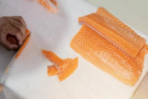 The salmon is in the hands of the experienced chef, using a knife to slice .. Stock Photos