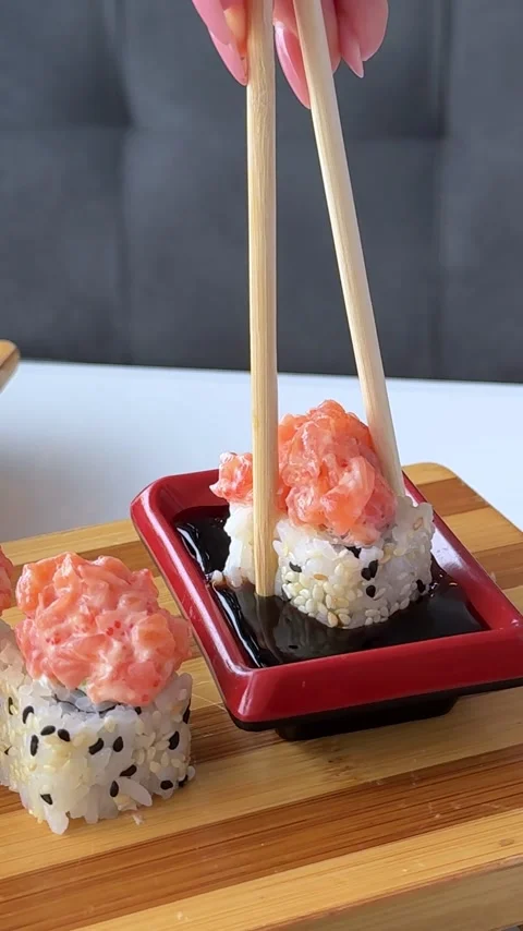 Salmon topped sushi roll with black sesame dipped into soy sauce in red Stock Footage 346186334