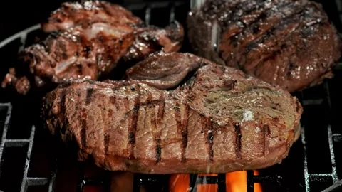 Salt falling on a grilled steak on a metal grate over an open fire Stock Footage 259087698