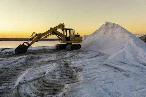 Salt farm excavator with sunset and a salt mountain Stock Photos