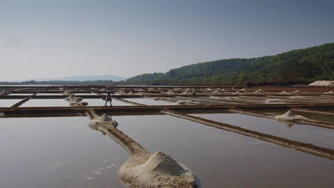 Salt Farming A Dedicated Worker Responsibly Tending to Expansive Salt Pans Under Stock Footage 303869878