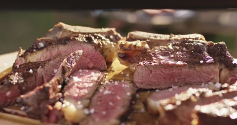 Salt flakes falling onto sliced grilled steak resting on a wooden cutting board Vídeo Stock 339977729