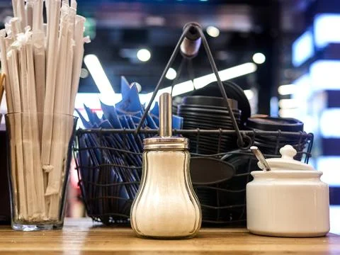 A salt shaker sits on a table next to a basket of napkins and a jar of sugar Stock Photos