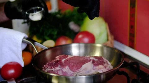 Salt sprinkled over beef steak by chef in black gloves while meat cooks in Stock Footage 346183446