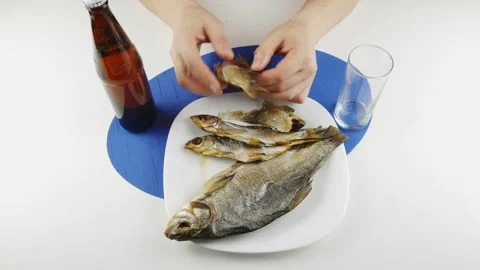 Salted dried fish on a white plate.Opens bottle and pours beer into a glass. Video stock 130637230