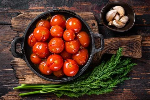 Salted Pickled cherry tomatoes in a pan with herbs and dill. Dark wooden Stock Photos