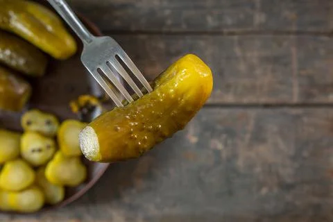 Salted pickled cucumbers on a fork in the foreground. in the background a pla Stock Photos
