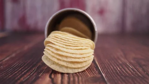 Salty potato chips falling out of silver container on wooden table in close.. Stock Footage 332144079